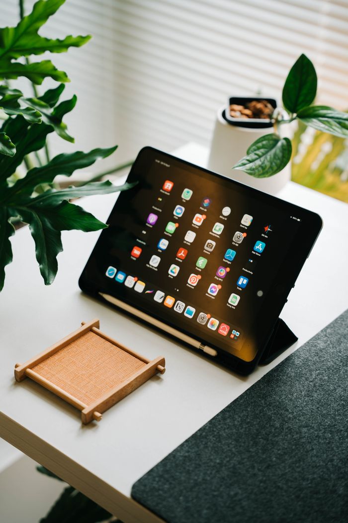 Home Tablet on a desk surrounded by plants in a modern workspace setting.